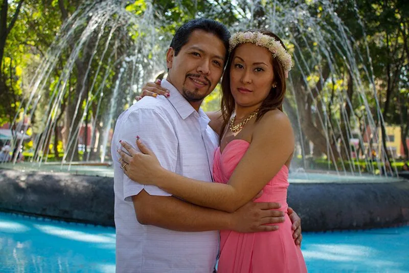 Pareja abrazada frente a una fuente en un parque.